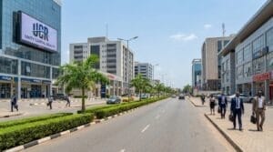 A street-level daytime photograph of the Wuse 2 commercial district in Abuja, showing a wide dual carriageway lined with modern office buildings, banks, and retail shops.